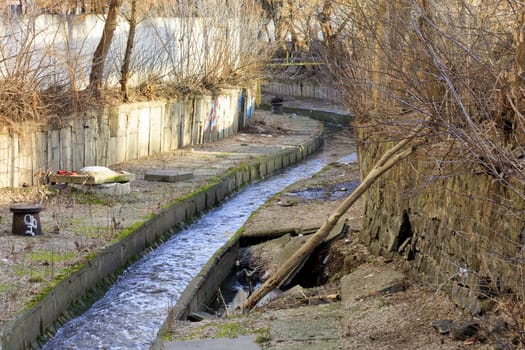 The dirty river Lybid flows along an old, damaged, worn-out channel enclosed in a concrete chute. Ecological disaster of the modern city.