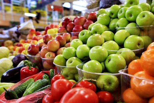 Bright background of fresh fruits. Green, red, yellow apples, tomatoes, cucumbers, pepperslie in the trays in the market and attract attention.