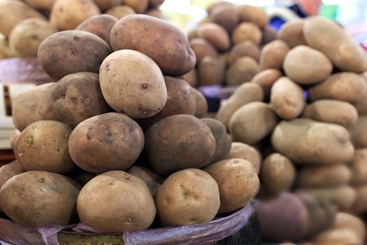 Closeup of dry potato tubers piled on market stalls in daylight.