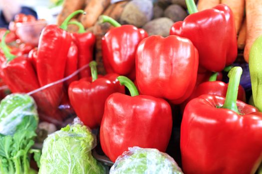 Large ripe red sweet bell peppers close-up on the background of other vegetables are sold in trays on the market in daylight.