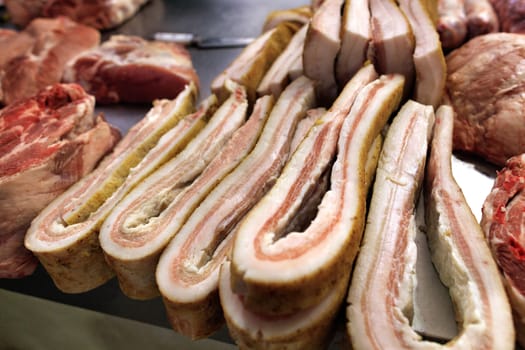 Fresh salted bacon and sliced pieces of meat are on the counter for sale in the market.