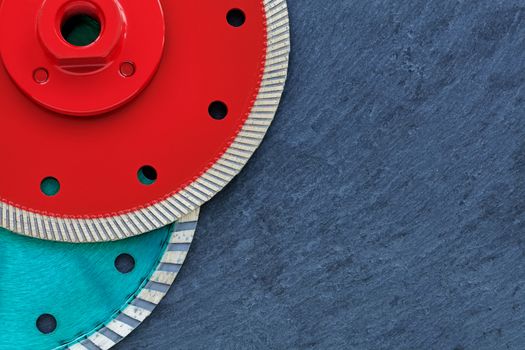 Several diamond cutting wheels of red and emerald color are located on top of each other against the background of gray granite close-up.