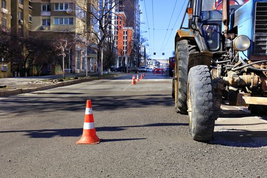 Orange traffic cones and an old tractor enclose a road repair area on a city street