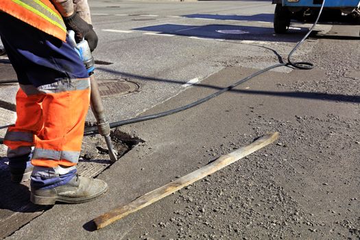 A road maintenance worker removes old asphalt on the roadway with a jackhammer into an excavator during road construction.