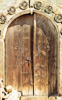 Very old weathered arched antique wooden doors with a stone pattern and metal wrought-iron lock.