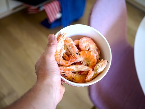 Bowl filled with fresh shrimps in man hands. Chairs are visible in the blurred background. Food for diet - Grilled shrimps with mango salad. Home cook in Asian kitchen.