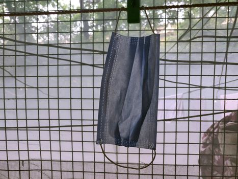 A surgical mask hanging by clothes pin near a grilled window during lock down in India