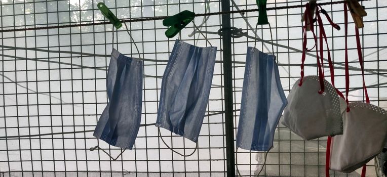 A series of N-95 and surgical mask hanging by clothes pin near a grilled window during lock down in India