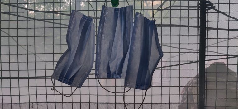 Three surgical mask hanging by clothes pin near a grilled window against smoke during lock down in India