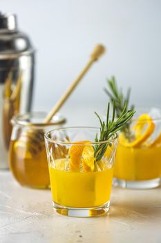 Honey bourbon cocktail with rosemary simple syrup or homemade whiskey sour cocktail drink with orange and rosemary. Decorate orange peel. Light concrete surface.