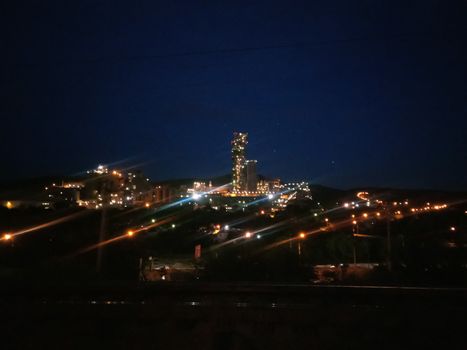 A large cement factory, kind of at night, lamps are lit.