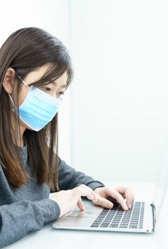 Woman using a laptop computer on the desk at home and wearing protective mask for protection against virus Covid-19