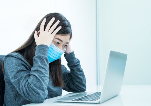 Woman using a laptop on the desk with headache and wearing  protective mask for protection against virus Covid-19