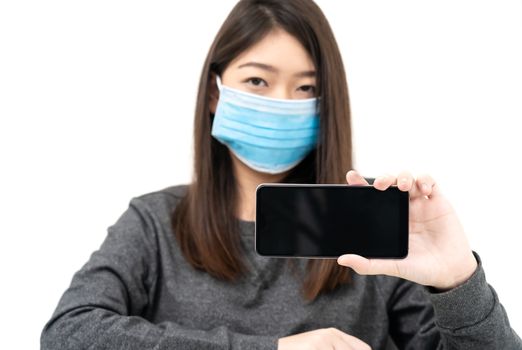 Close up woman wearing protective mask holding and showing mobile phone with blank black screen on white background