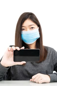 Close up woman wearing protective mask holding and showing mobile phone with blank black screen on white background