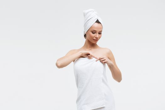 Sensual woman in fluffy white towel on head looking at finger touching towel on body