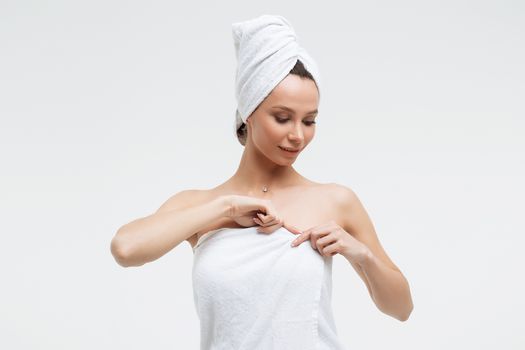 Sensual woman in fluffy white towel on head looking at finger touching towel on body
