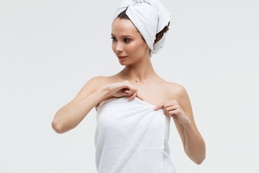 Sensual woman in fluffy white towel on head looking at finger touching towel on body