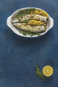 Mackerels served on white dish with lemon, thyme, rosemary and spices. Raw marinated fishes on classic blue surface. Seafood flat lay background with copy space for you text.