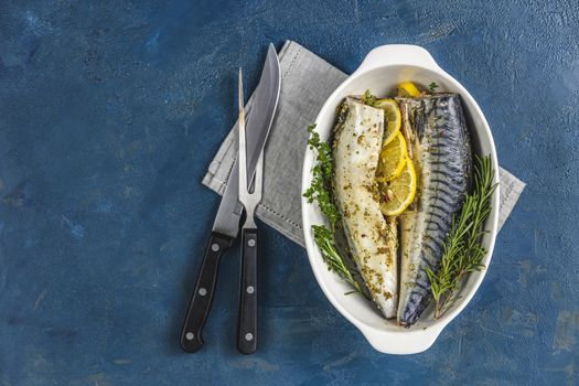 Mackerels served on white dish with lemon, thyme, rosemary and spices. Raw marinated fishes with cutlery on classic blue surface. Seafood background.