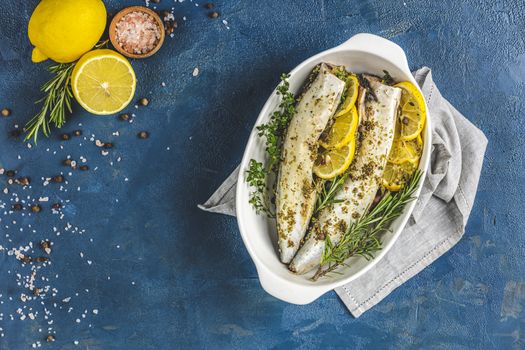 Mackerels served on white dish with lemon, thyme, rosemary and spices. Raw marinated fishes on classic blue surface. Seafood background.