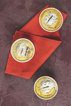 Three apple pies in ceramic baking molds with napkin ramekin on dark red concrete table. Top view, flat lay.