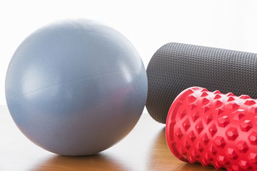 A blue ball and a grey pilates roller and a red fascial massage roller, with backlight and wooden floor