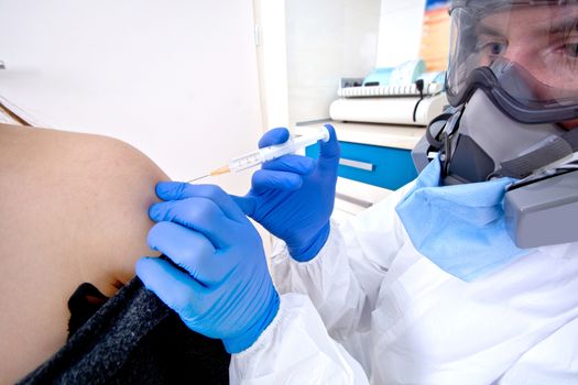 Doctor in protective suit uniform and mask giving a vaccine to female patient. Coronavirus outbreak. Covid-19 concept.