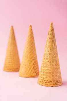 Three upside down wheat flour ice cream cones diagonally towards the bottom on a pink background. Summer concept.