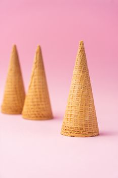 Three wheat flour ice cream cones upside down one in the foreground and the other in the background on a pink background. Summer concept.