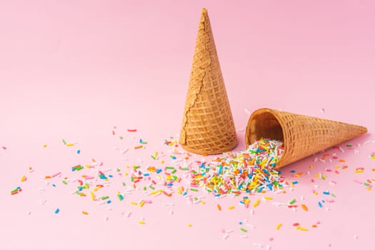 Two wheat flour ice cream cones one upside down and the other filled with colored sugar on a pink background. Summer concept.