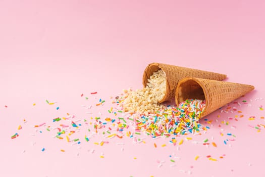 Two wheat flour ice cream cones one filled with roasted, natural and granulated almonds and the other filled with colored granulated sugar on a pink background. Summer concept