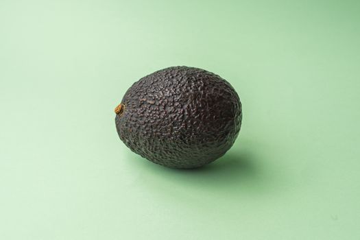 Whole and ripe natural avocado with rough skin located in the center with a green background. Natural fat and raw food