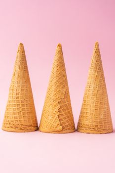 Three upside down wheat flour ice cream cones lined up towards the bottom on a pink background. Summer concept