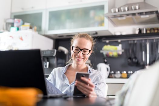 Stay at home and social distancing. Woman in her casual home clothing working remotly from kitchen dining table. Video chatting using social media with friend, family, business clients or partners.