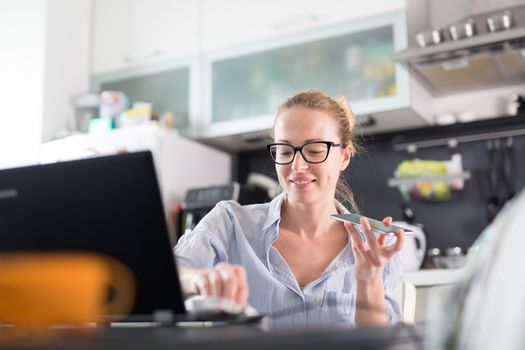 Stay at home and social distancing. Woman in her casual home clothing working remotly from kitchen dining table. Video chatting using social media with friend, family, business clients or partners.