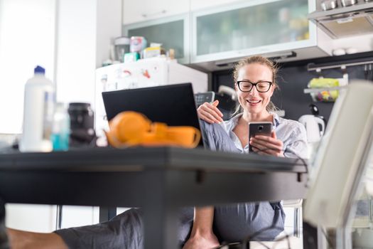 Stay at home and social distancing. Woman in her casual home clothing working remotly from kitchen dining table. Video chatting using social media with friend, family, business clients or partners.