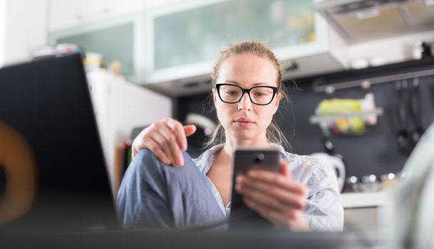 Stay at home and social distancing. Woman in her casual home clothing working remotly from kitchen dining table. Video chatting using social media with friend, family, business clients or partners.