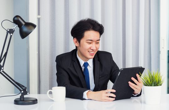 Work from home, Asian young businessman video conference call or facetime he smiling looking to camera sitting on desk using smart digital tablet computer touching on screen at home office