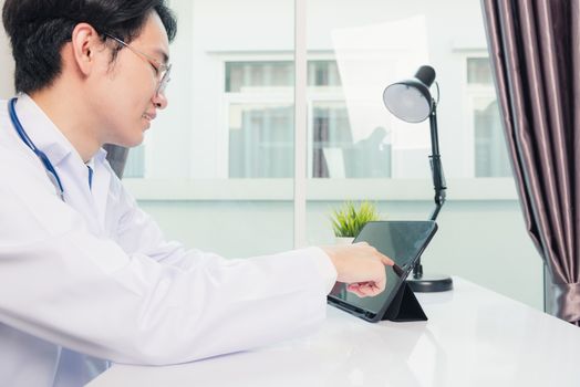 Happy Asian young doctor handsome man smile work from home office wear glasses, using black modern smart digital tablet computer on desk at hospital office, Technology healthcare and medicine concept