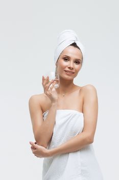 Charming pleasant woman in fluffy white towel on head with glass of clean water looking away touching towel on body