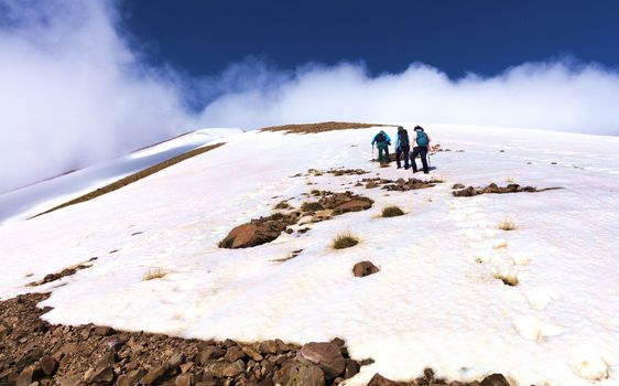 A group of tourists with backpacks on their backs goes hiking on a rocky snow-covered slope to the misty top of Erciyes mountain in Turkey.