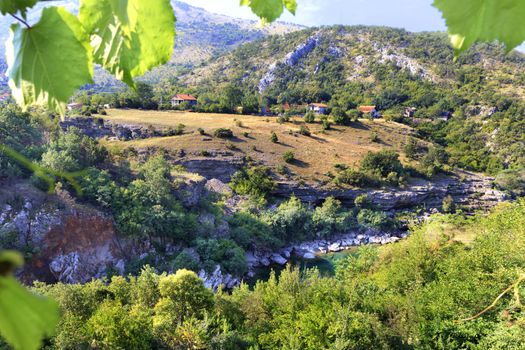 The clear turquoise water of a mountain river flows between rocky shores and stone rapids in the countryside of central Montenegro.