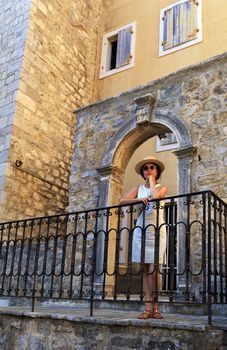 Woman in sun glasses and straw hat. Fashion. A beautiful lady in a straw hat is standing on the porch of an old house against the background of an openwork antique arch.