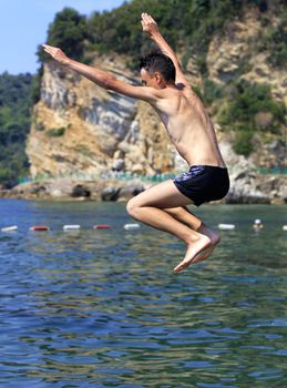 Brave teenager jumps from a cliff into the sea against the backdrop of defensive coastline buoys