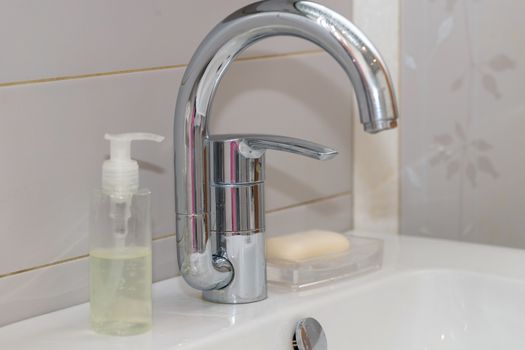 Modern hand wash basin. Solid tabletop surface and gray tile wall. Dispensable soap next to water tap on bathroom sink