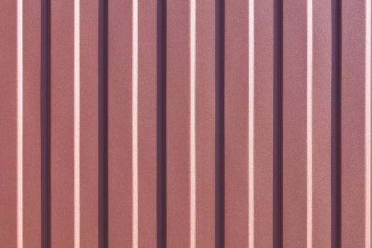 Brown metallic fence made of corrugated steel sheet with vertical guides. Corrugated brown iron sheet background close up.