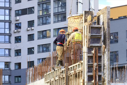 Workers poured concrete in the formwork of the walls on the construction of the house against the background of a modern residential building.