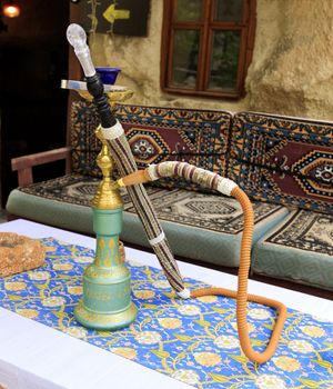 Hookah stands on the table on a beautiful white and blue tablecloth with oriental ornaments in an old hut on the background of a blurred interior