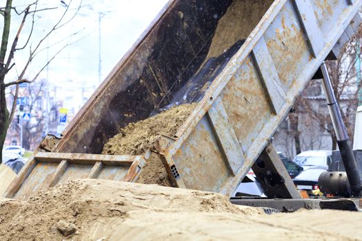 At the construction site of a city street, a cargo truck dumps sand.